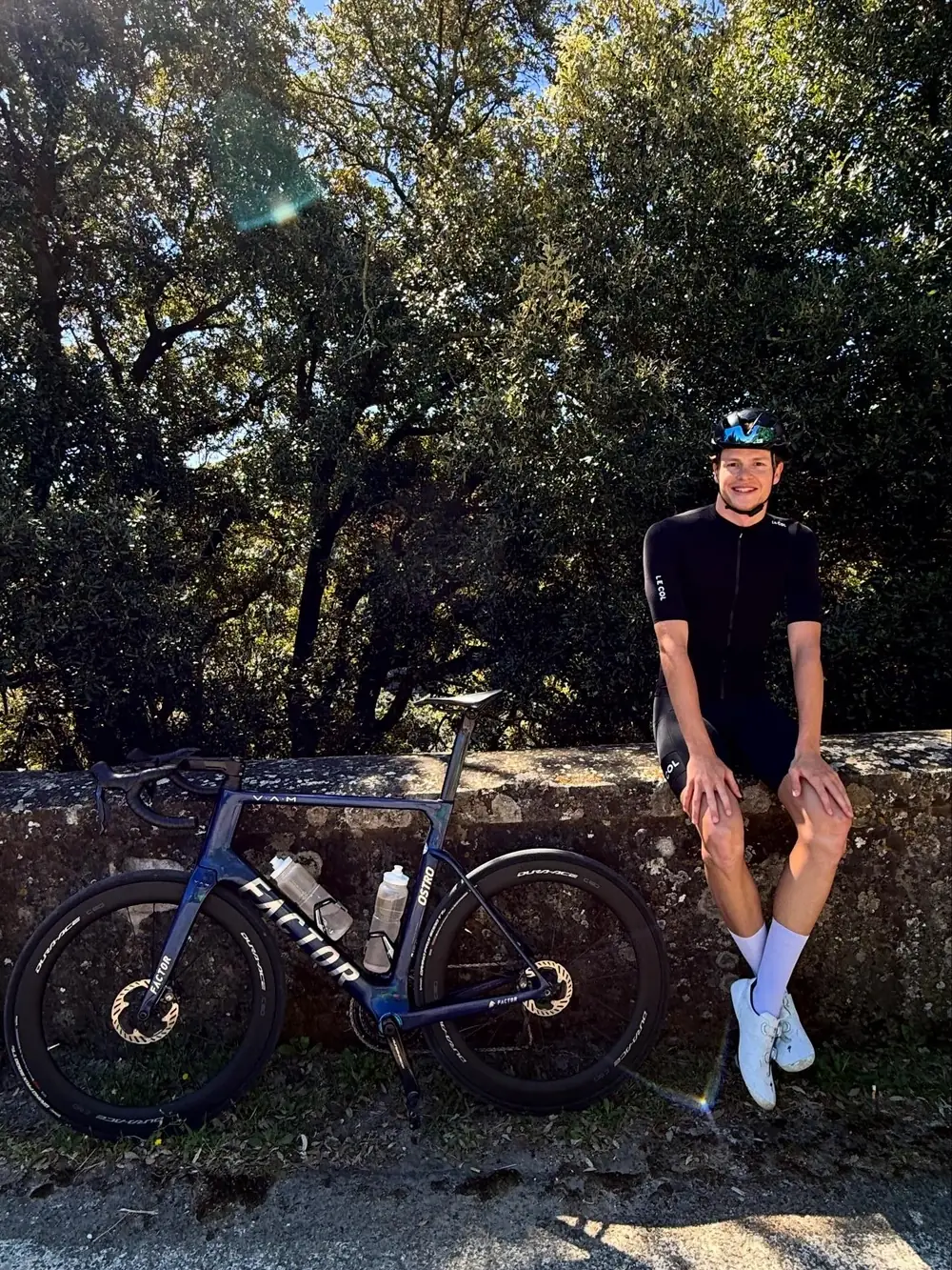 Thomas sitzt auf einer Steinmauer neben seinem Rennrad